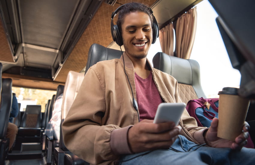 a charter bus passenger listens to music on his phone with over-ear headphones