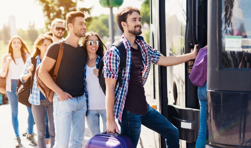 a line of passengers take turns loading their charter bus rental