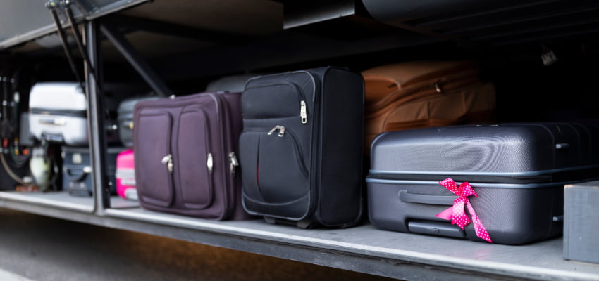 various suitcases in a charter bus luggage bay. one black suitcase has a pink bow tied to the handle