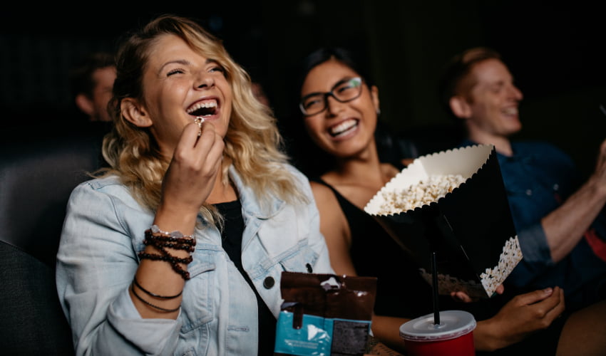 two film enthusaists laugh and share popcorn in a theater