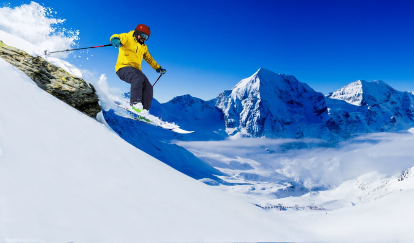 a skier in a yellow jacket performs a jump from a small cliff