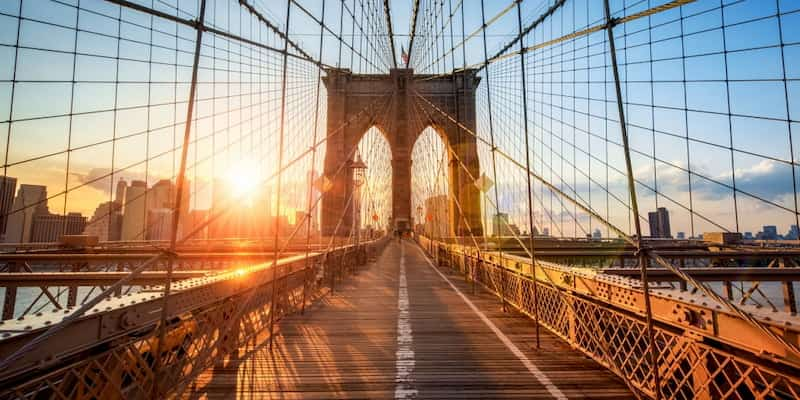 the sun sets over the pedestrian path on the brooklyn bridge in new york city