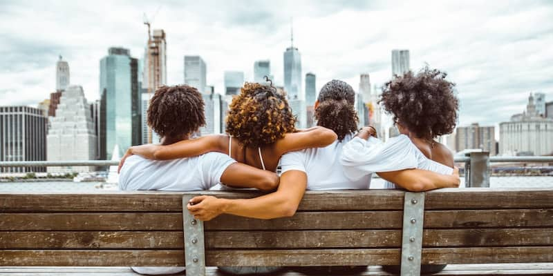 a group of friends sit on a bench in a new york city borough and look at the skyline