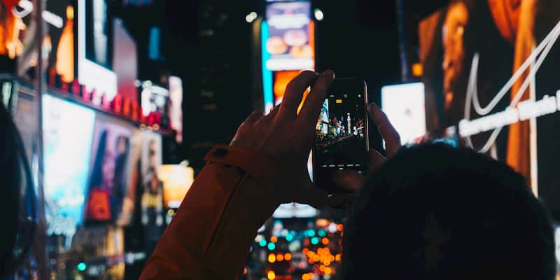 a tourist takes a photo on their phone in time square in new york city