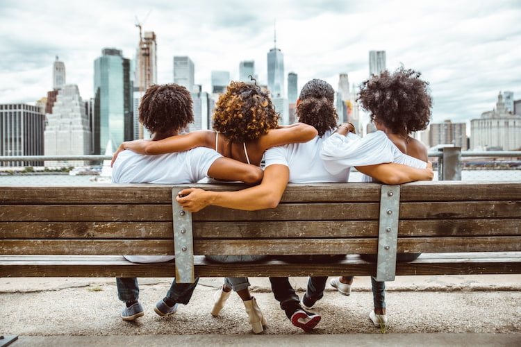a group of friends sit on a bench in a new york city borough and look at the skyline
