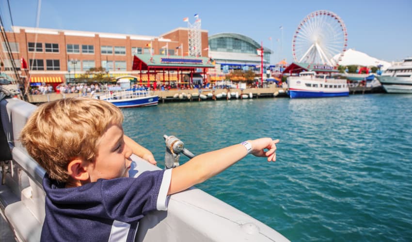a small boy laughs and points at the Ferris wheel at Chicago's Navy Pier