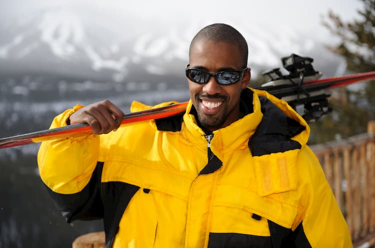 Man holding skis in yellow jacket