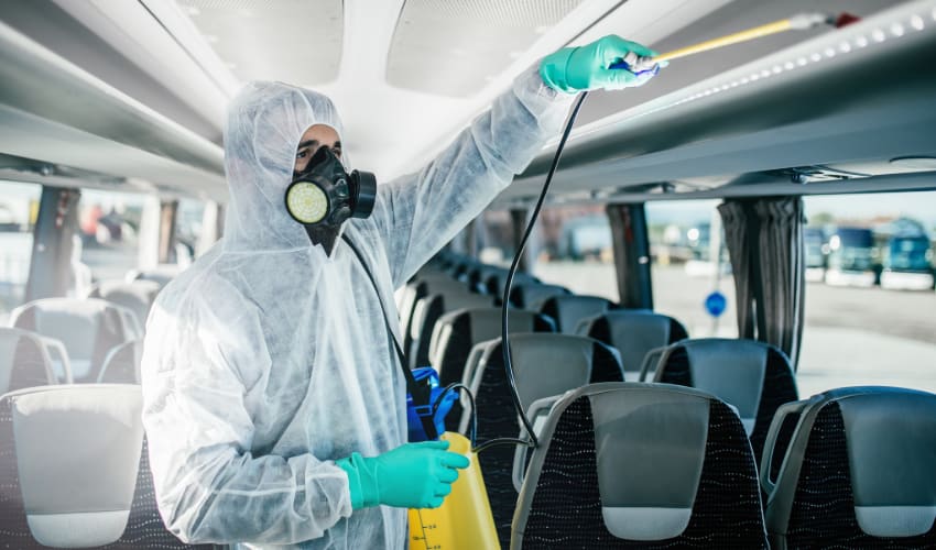 A person in a hazmat suit disinfects a charter bus interior
