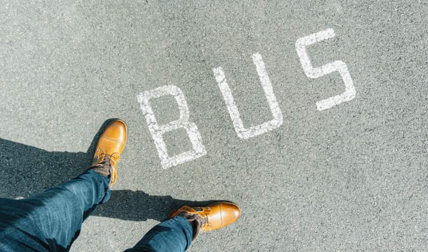 Top-down view of feet standing new the word "bus" painted on a city street