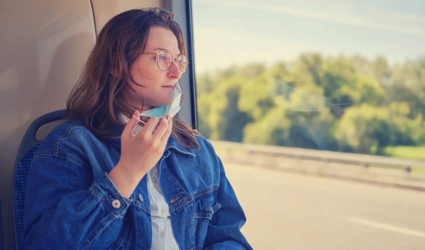 A woman ride in a charter bus and puts on a disposable mask