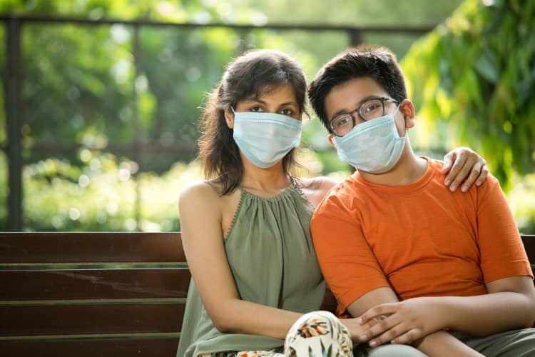 Two people sitting on a bench while wearing face masks