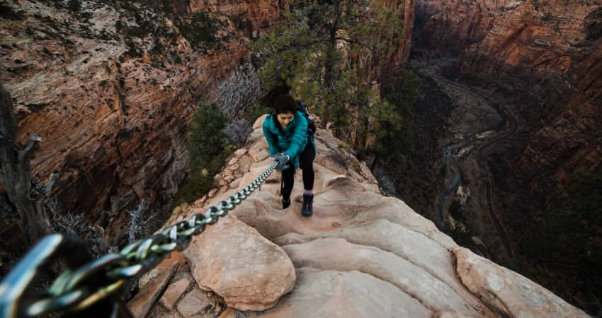 A woman holds on to a chain railing along the narrow ridge of Angel's Landing in Zion National Park