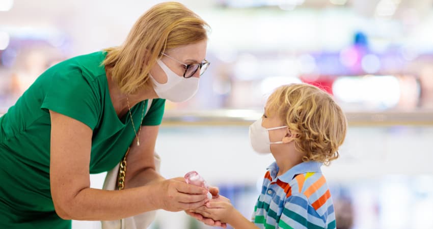 A woman and child wearing masks and using hand sanitizer