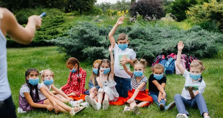 A group of children wearing masks and sitting in a garden