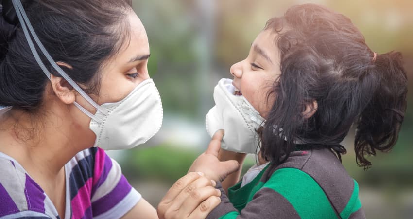 A woman helping a child adjust a face covering 