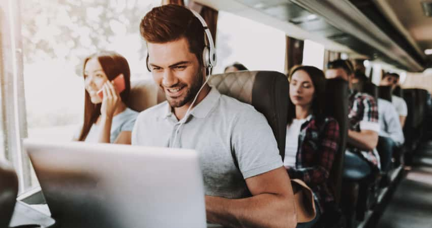 A group of young people on a coach bus including someone using a laptop and headphones