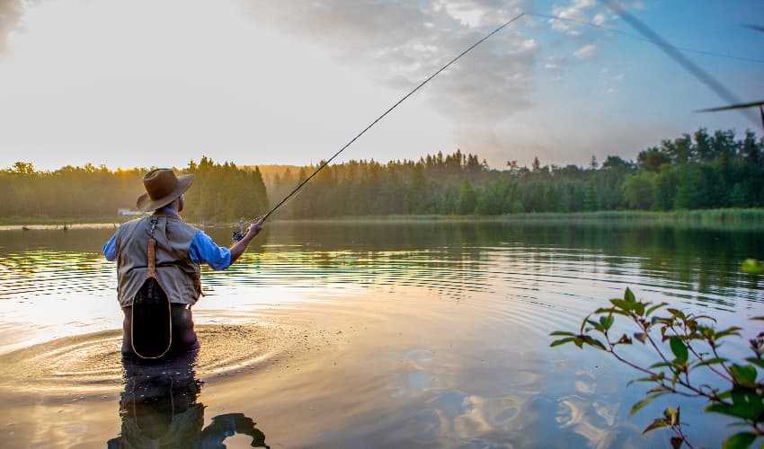 A fly fisherman casts his reel on a peaceful lake at sunrise