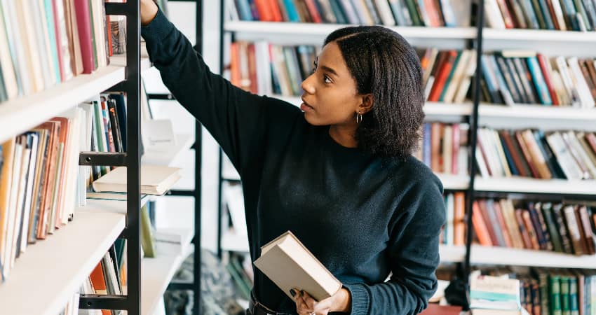 A woman grabs books off a crowded shelf in a bright book store