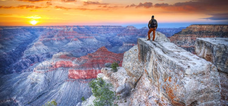 a man stands at a rock summit overlooking the vast and colorful grand canyon