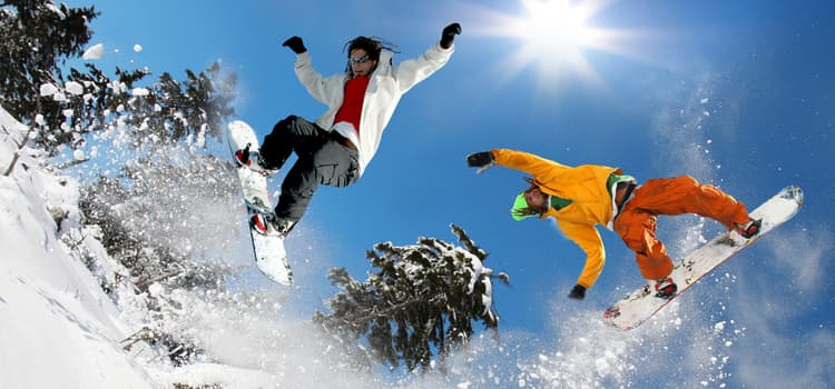 two friends jump over a slope on snowboards while snow flies into the air