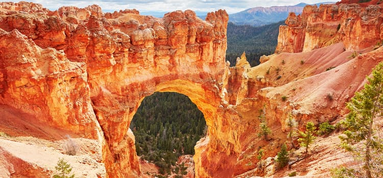 a natural rock arch at bryce canyon with green trees in the background