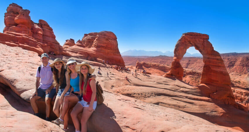 A family taking a photo in front of Delicate Arch at Arches National Park
