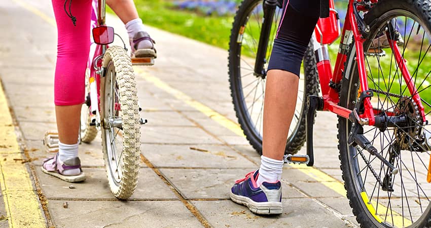 An adult and child mount bicycles on an urban trail