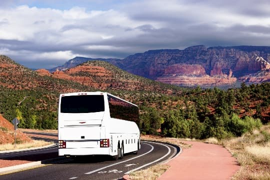 A white charter bus traveling on a road with hills in the background