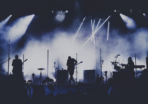 silhouettes of band members on a dark stage with bright spotlights
