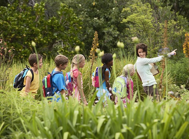 A class of students and a teacher walk through a green field with backpacks