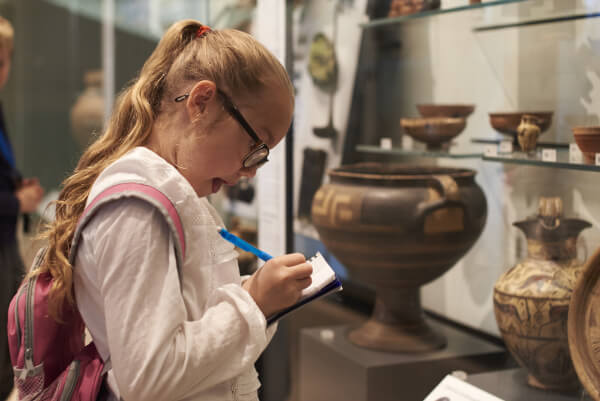 a young girl makes notes in front of an exhibit at a museum