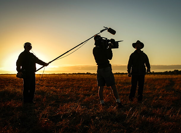A film crew stands in an empty field at sunset