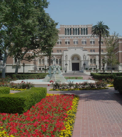 A red and yellow flower bed and a fountain in front of the USC library
