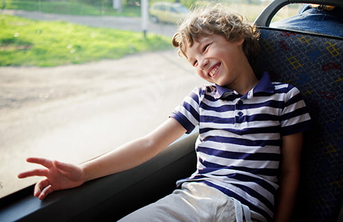 A child smiles and looks out the window of a bus rental