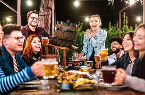 friends smile and hold up their beers after dark at a beer garden