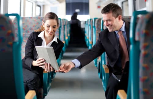two business professionals look over a tablet device on a charter bus