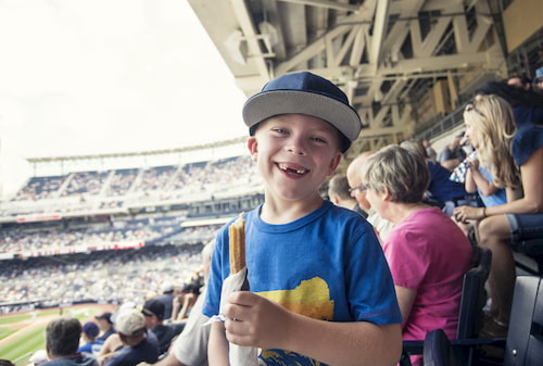 young boy smiles while standing in a crowd of baseball fans