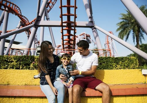 family laughing and smiling near an amusement park roller coaster