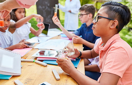 A group of students perform a science experiment with test tubes in an outdoor setting