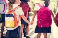 two young students wearing backpacks hold hands