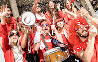 marching band members cheer and dance while dressed in red at a game