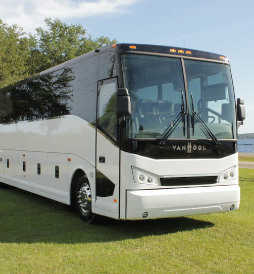 A white Van Hool charter bus parks in a grassy field