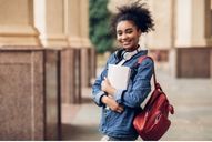 female student smiling and holding books and a backpack