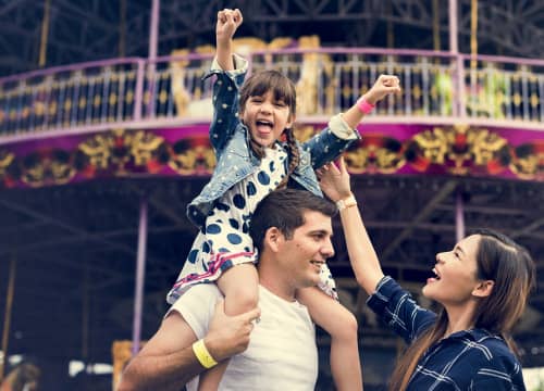 kid holds up arms in excitement at amusement park